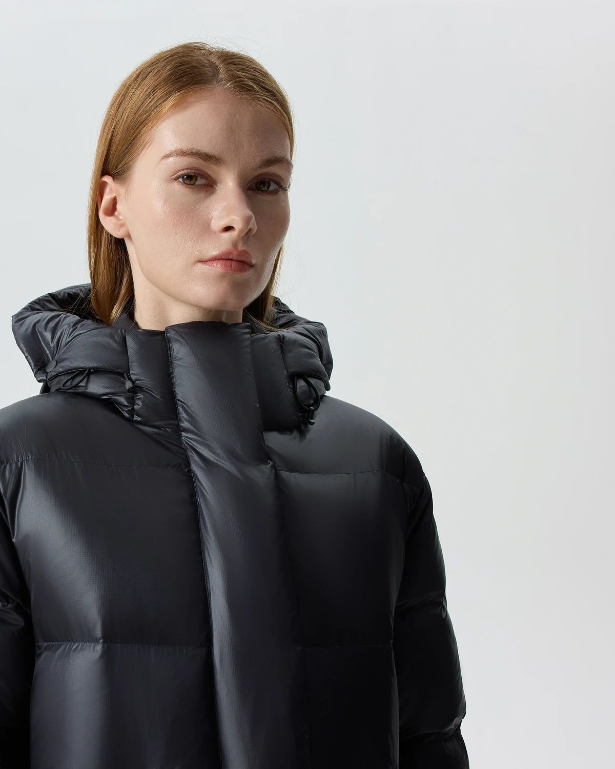 A close portrait of a woman wearing the high collar of a black Waukee long down puffer.